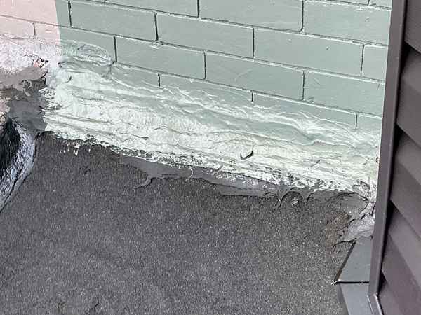 Roofing cement used as temporary flashing at a flat roof-to-wall joint
