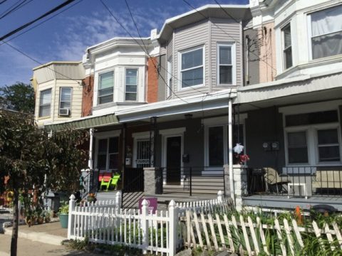 Typical Philadelphia row homes with front porches, white picket fence, and colorful chairs on a sunny day.