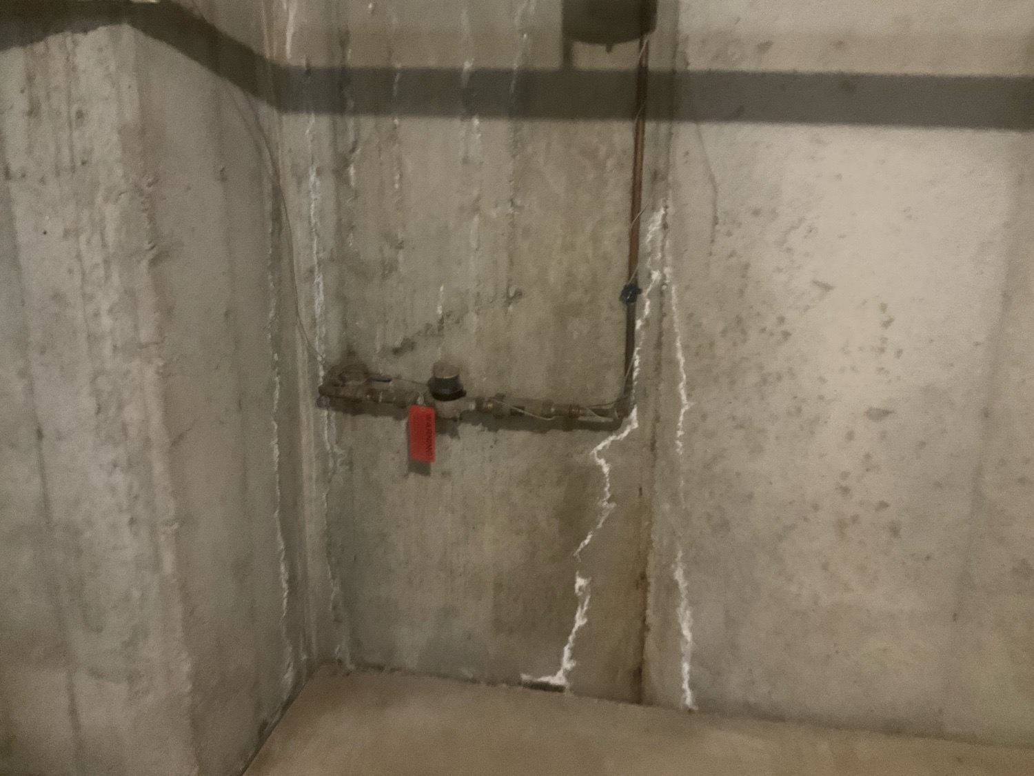 Basement corner during DIY home inspection showing white efflorescence staining and mineral deposits on concrete walls — clear signs of moisture penetration.