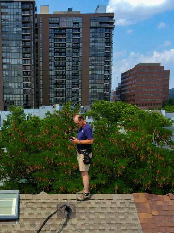ValueGuard home inspector on a Philadelphia rooftop inspecting shingles and a skylight, with the city skyline behind.