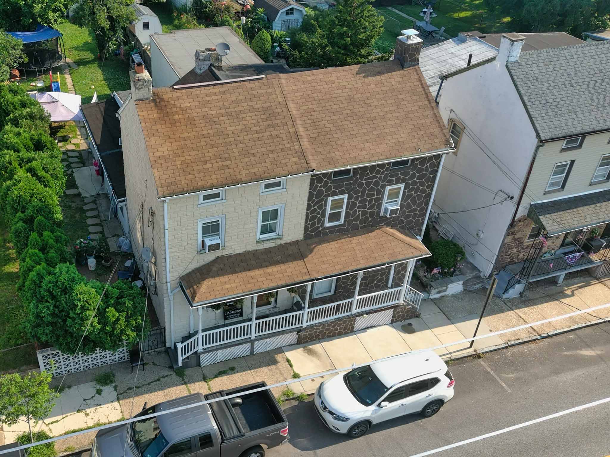 Aerial view of an older twin home refaced with simulated stone veneer over brick, painted side wall and a full-width shed-roof front porch in Phoenixville, Chester County PA, inspected by ValueGuard home inspectors