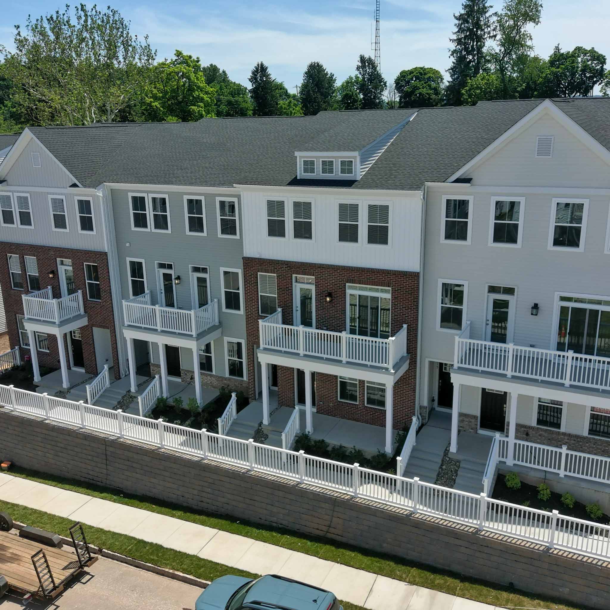 Aerial view of a row of new three-story townhomes with brick and siding facades, private balconies and white vinyl fencing in Phoenixville, Chester County PA, inspected by a ValueGuard home inspector