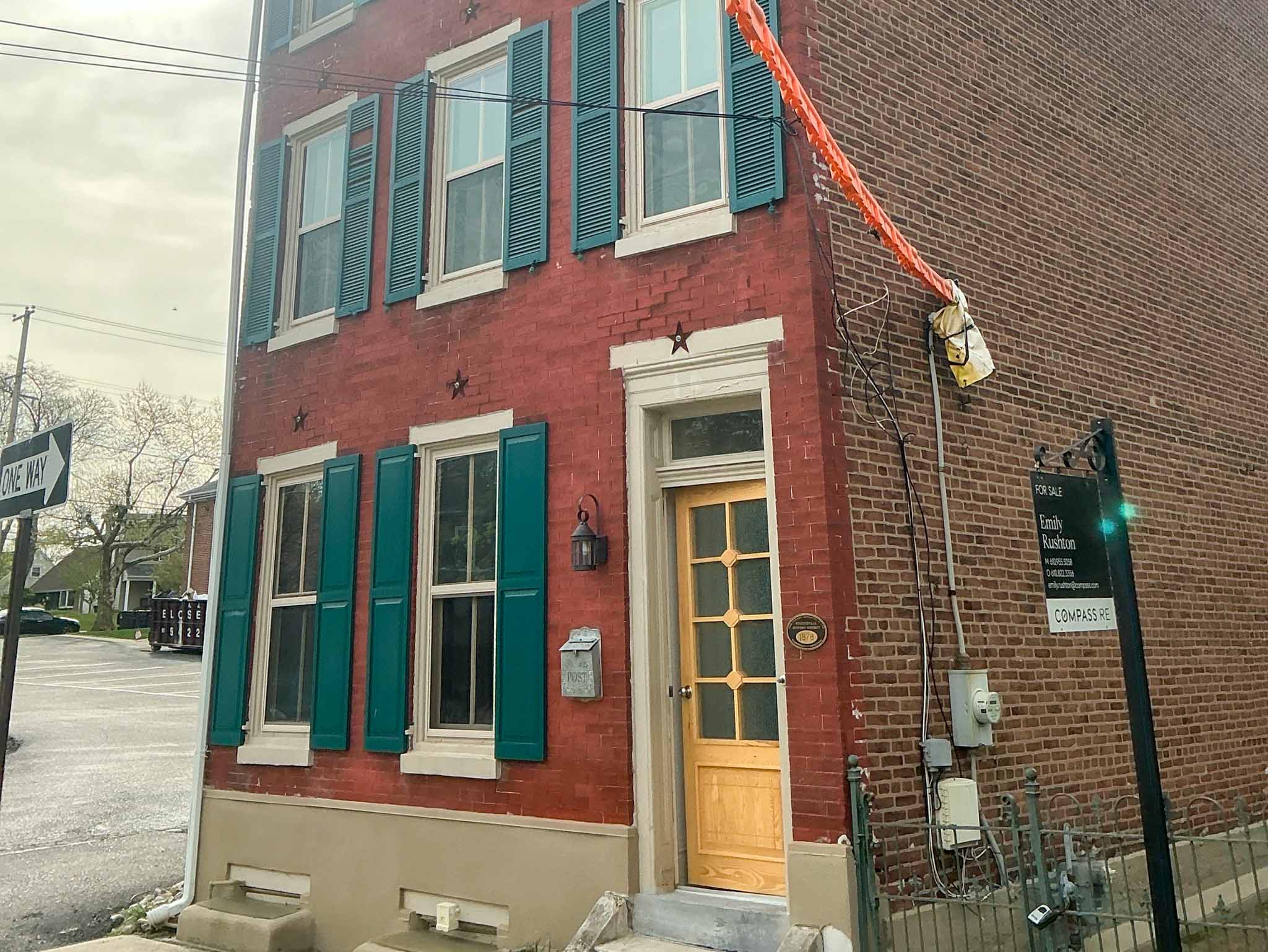 Historic red brick Borough rowhome dated 1878 with teal green shutters, transom entry door and overhead service wires in Phoenixville, Chester County PA, inspected by a ValueGuard home inspector