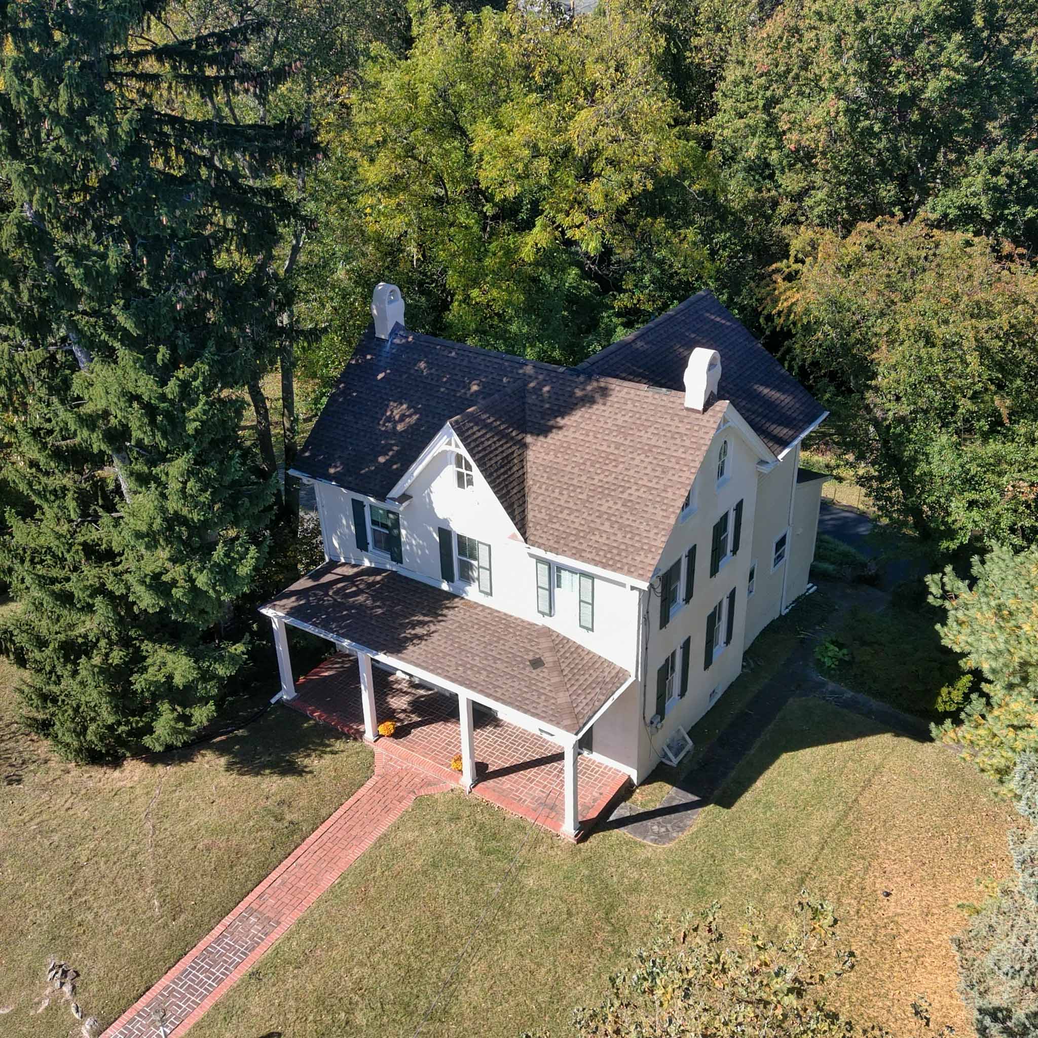 Aerial view of a white painted-stucco farmhouse colonial with a wraparound porch and shingle roof in Bala Cynwyd inspected by ValueGuard home inspectors