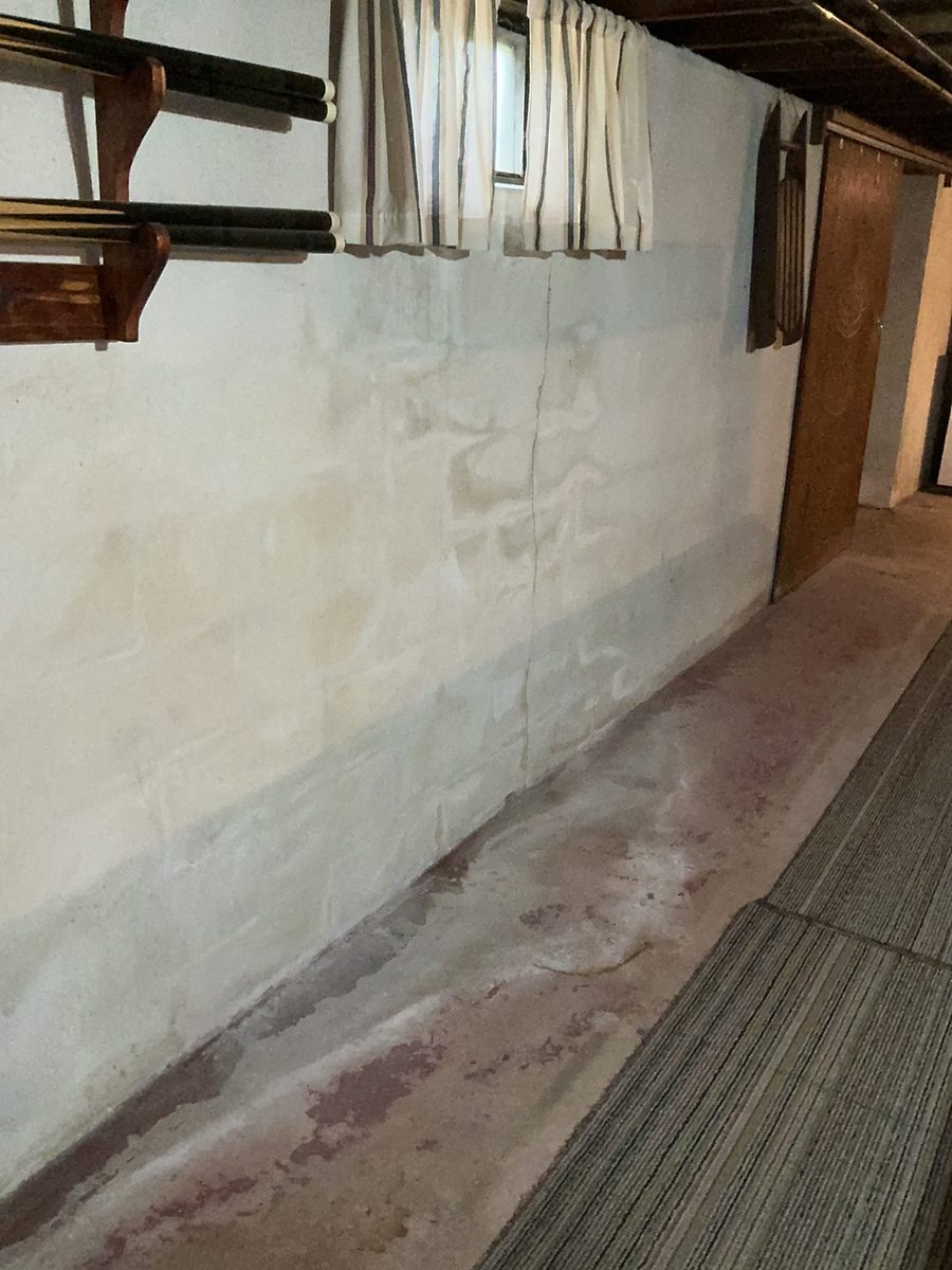 Water staining and white efflorescence along the base of a painted basement wall