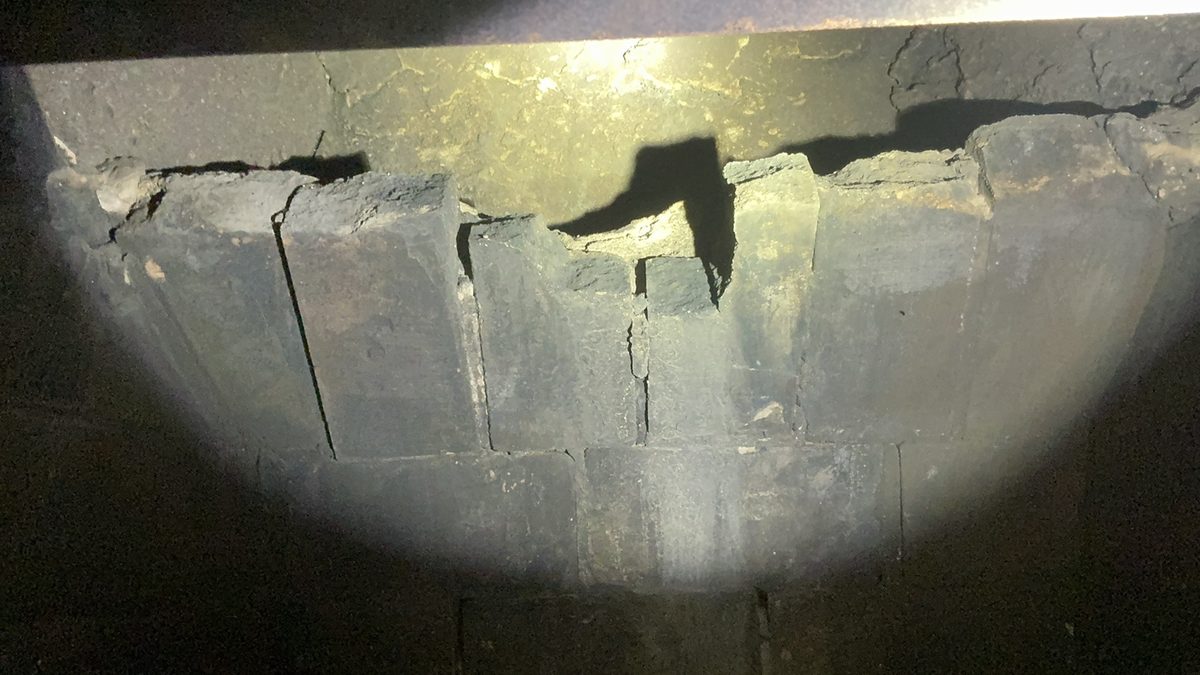 Cracked and displaced masonry above a fireplace firebox, seen with a flashlight