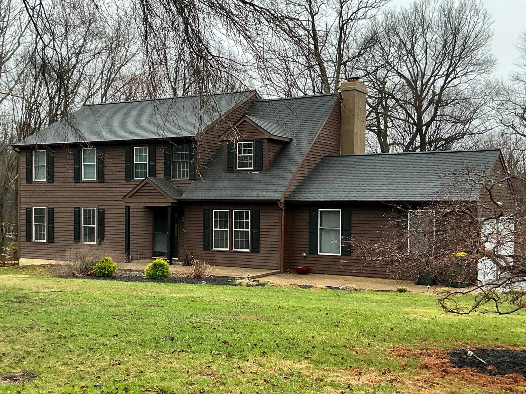Khaki clapboard colonial with a large two-story three-bay garage wing and brick chimney on a wooded lot in Downingtown, Chester County PA, inspected by ValueGuard home inspectors