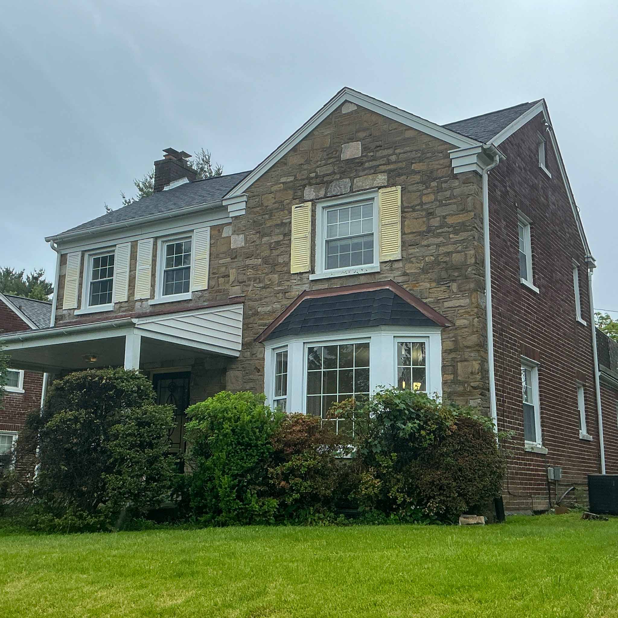 Stone-and-brick Elkins Park colonial with a shingle-roofed bay window and covered porch inspected by a ValueGuard home inspector