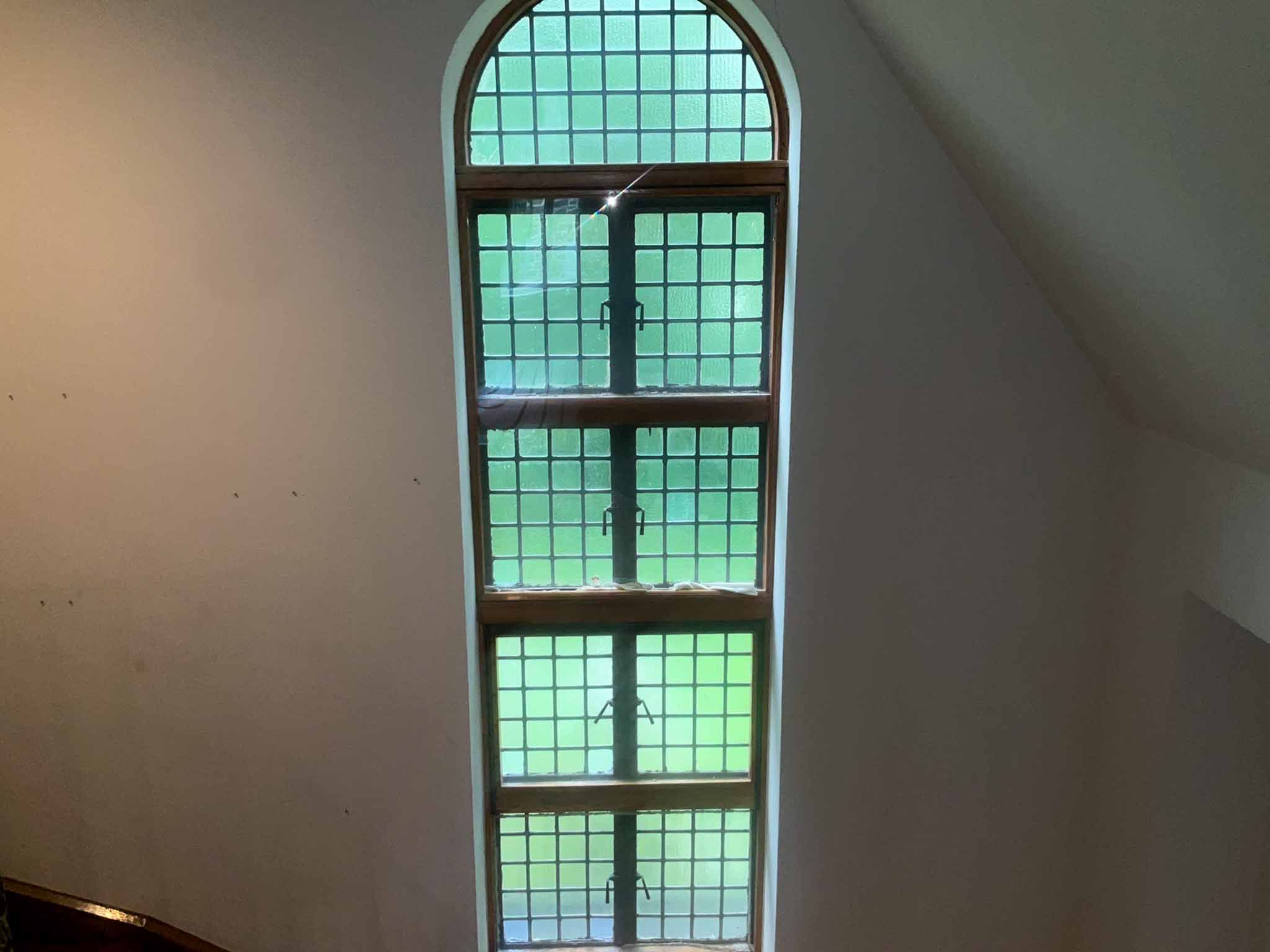 Tall arched leaded glass window with square panes in the stairwell of a 1927 Tudor Revival home in Wynnewood PA