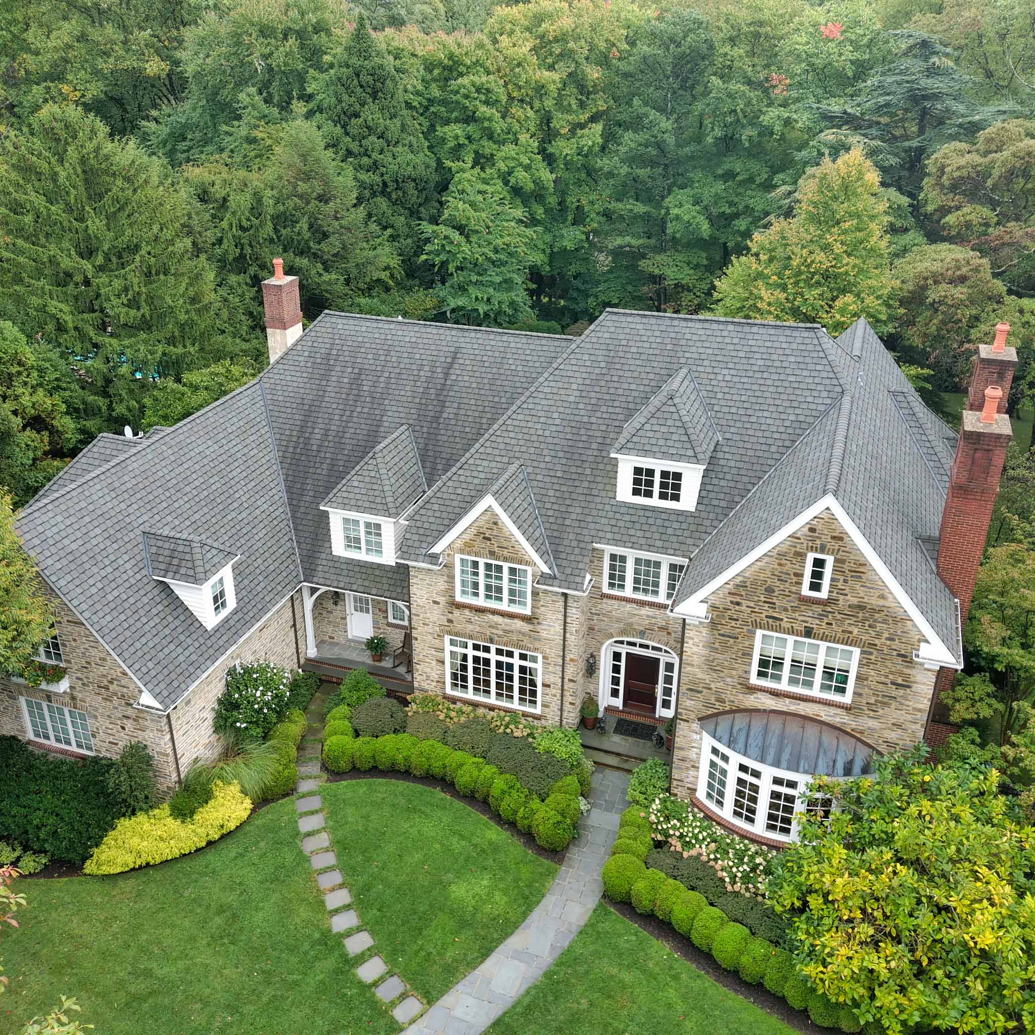 Aerial view of a stone Main Line home's roof, dormers, and brick chimneys during a ValueGuard home inspection in Pennsylvania