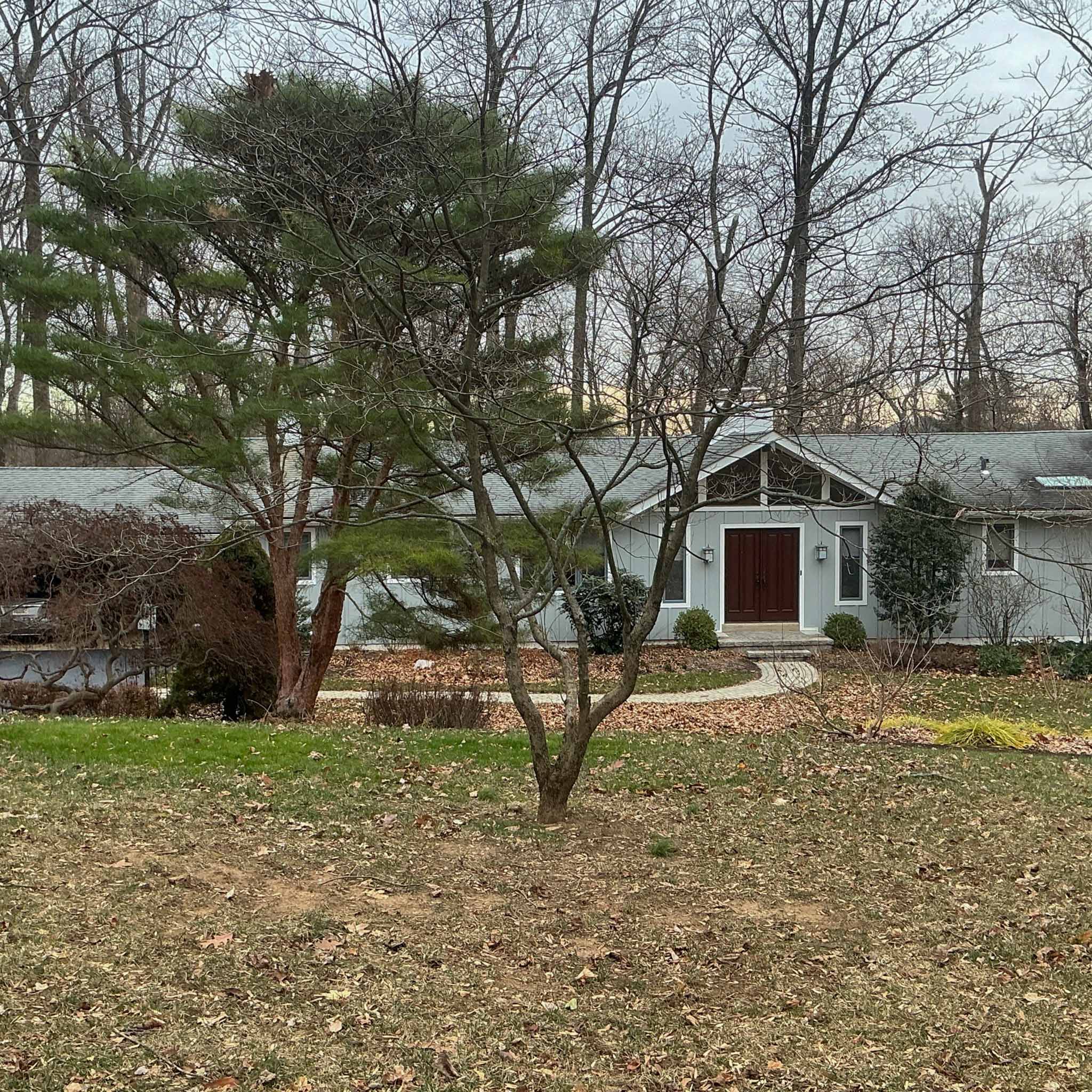 Newtown Square Home Inspection — Expanded Ranch Sprawling blue-gray expanded ranch with a gabled entry and red door on a wooded Newtown Square lot inspected by a ValueGuard home inspector