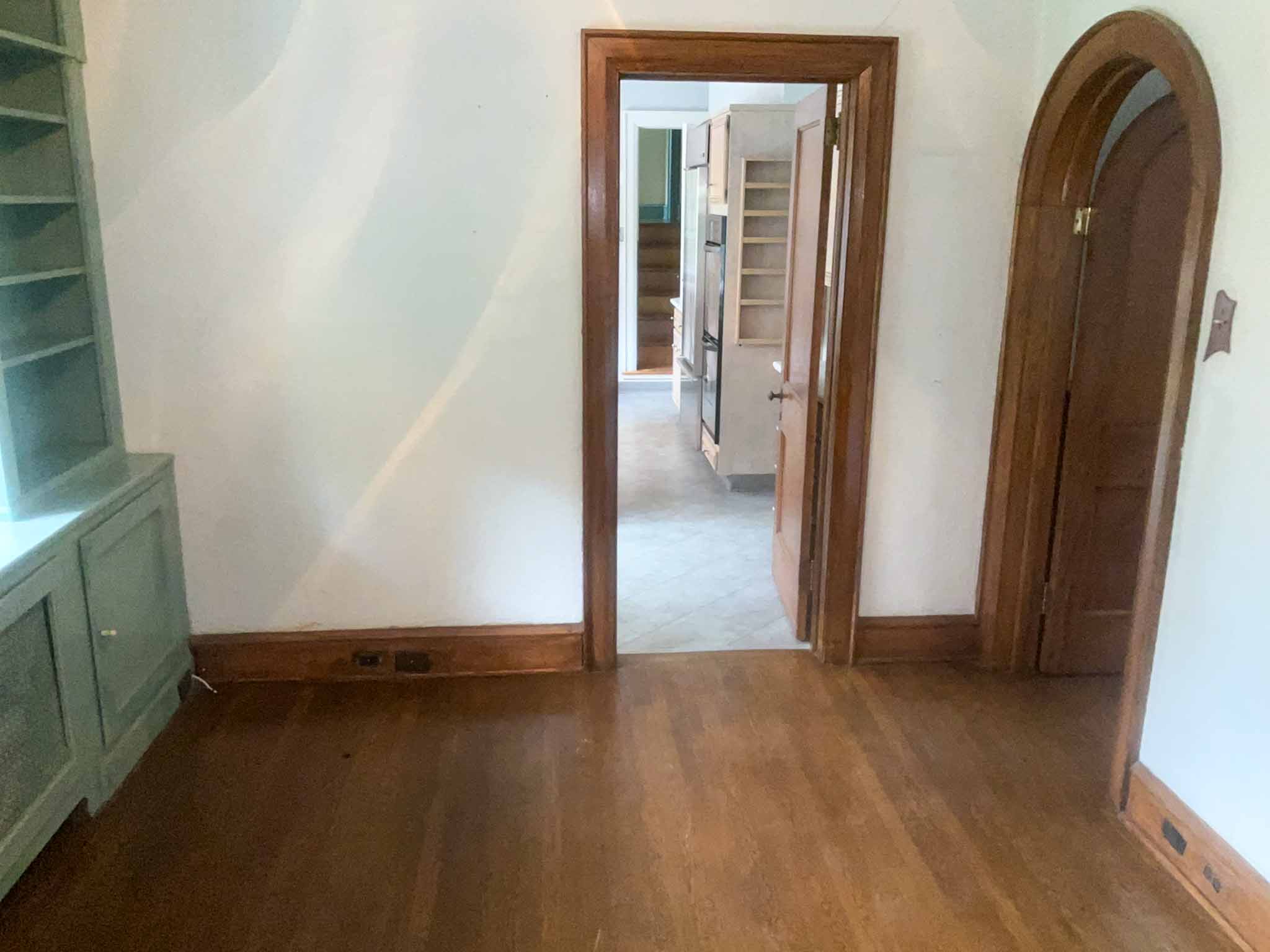 Interior of a Wynnewood Tudor Revival home showing an original arched oak door, stained wood trim, hardwood floors, and painted built-in shelving