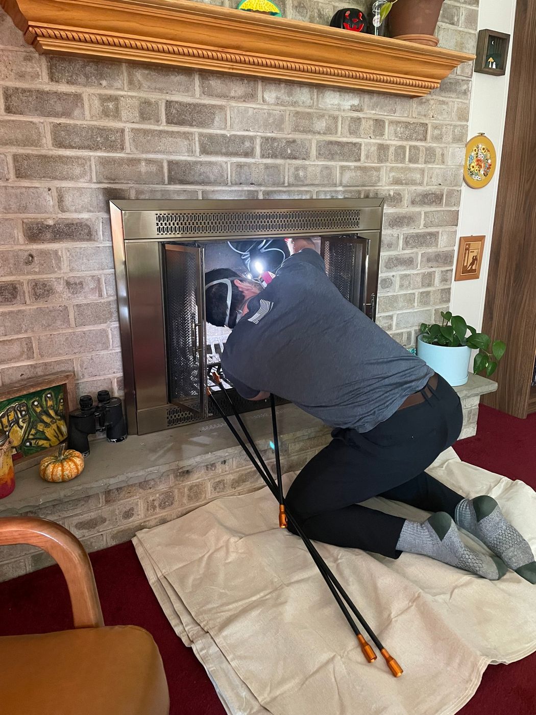 Tyler Gilger inspecting the firebox and damper of a fireplace with a headlamp and chimney rods during a Level 2 chimney inspection
