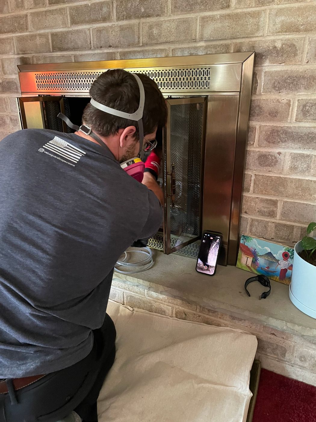 ValueGuard inspector Tyler Gilger running a video camera through a fireplace flue during a Level 2 chimney inspection, with the live camera feed showing the inside of the flue on the phone screen