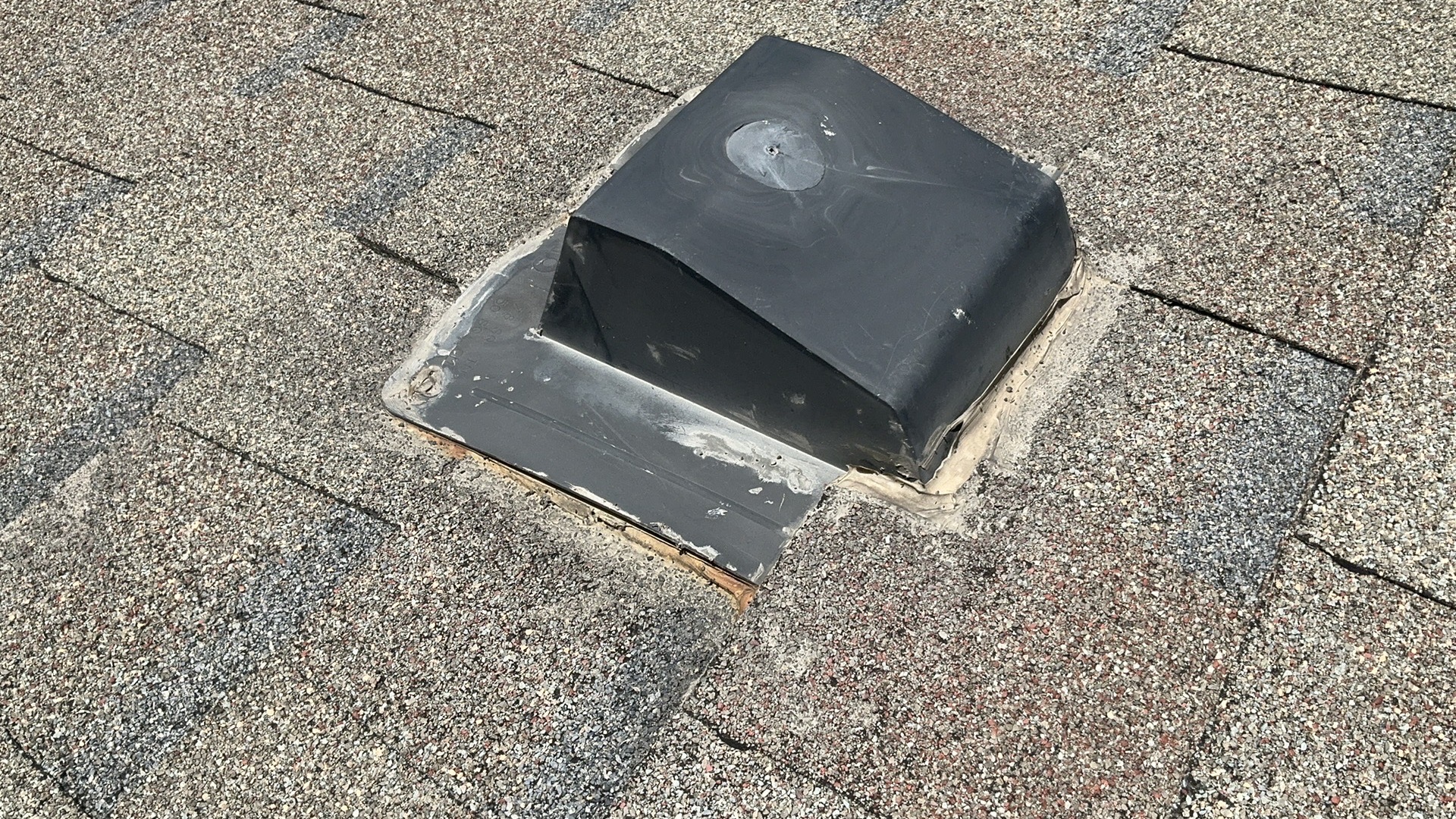 Close-up of a worn plumbing vent boot with old sealant on an asphalt shingle roof